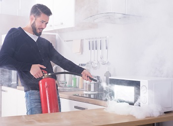 man holding a fire extinguisher and using it on his microwave in the kitchen